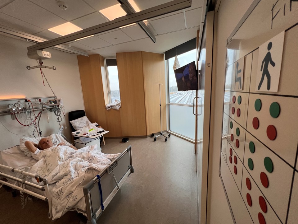 I forgrunden hænger magnettavlen på væggen. I baggrunden ligger Finn Jensen Eriksen i sengen