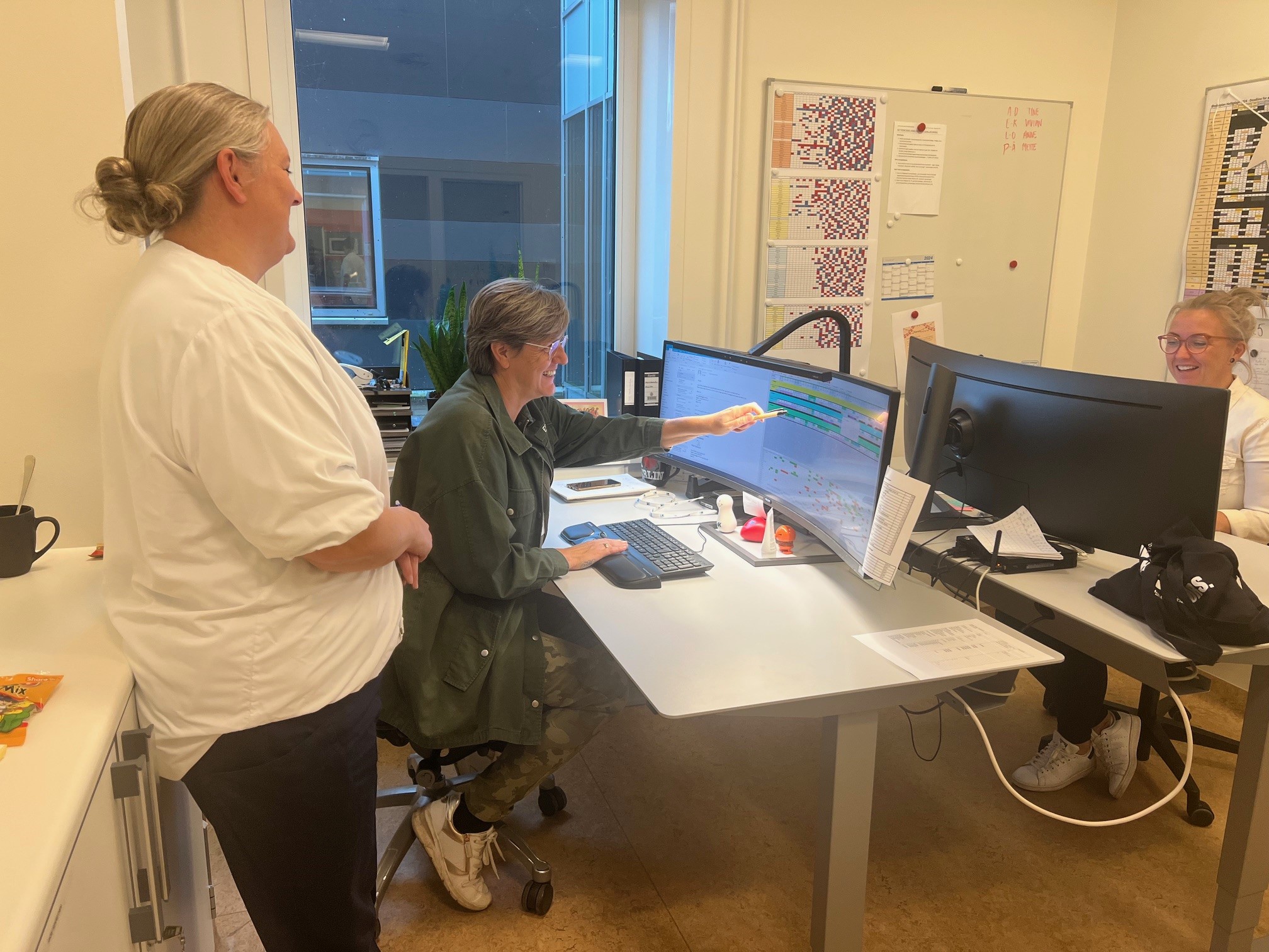 Oversygeplejerske Mette Lønborg Eriksen og FAMs to vagtplanlæggere, Ann Rosenkilde og Linda Hvenegaard, i fuld gang med planlægningen, mens oversygeplejerske Mette Lønborg Eriksen følger med på sidelinjen. 