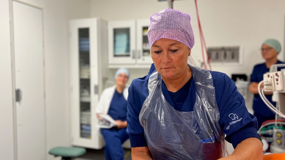 På et leje ligger en patient, som er ved at blive klargjort til en hofteoperation. Sygeplejerske Grethe Hjuler Jensen taler med patienten inden operationen.